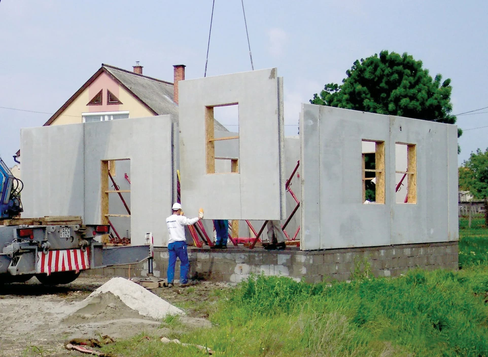 Kran hebt eine vorgefertigte Betonwandplatte mit Fensteröffnung auf einer Baustelle