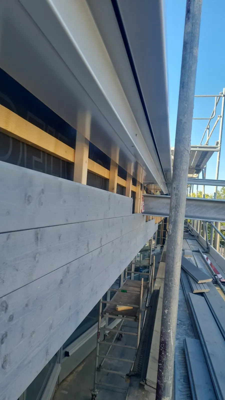 Gerüst mit Bohlen entlang einer Fassade, an der Fassadenpaneele montiert werden