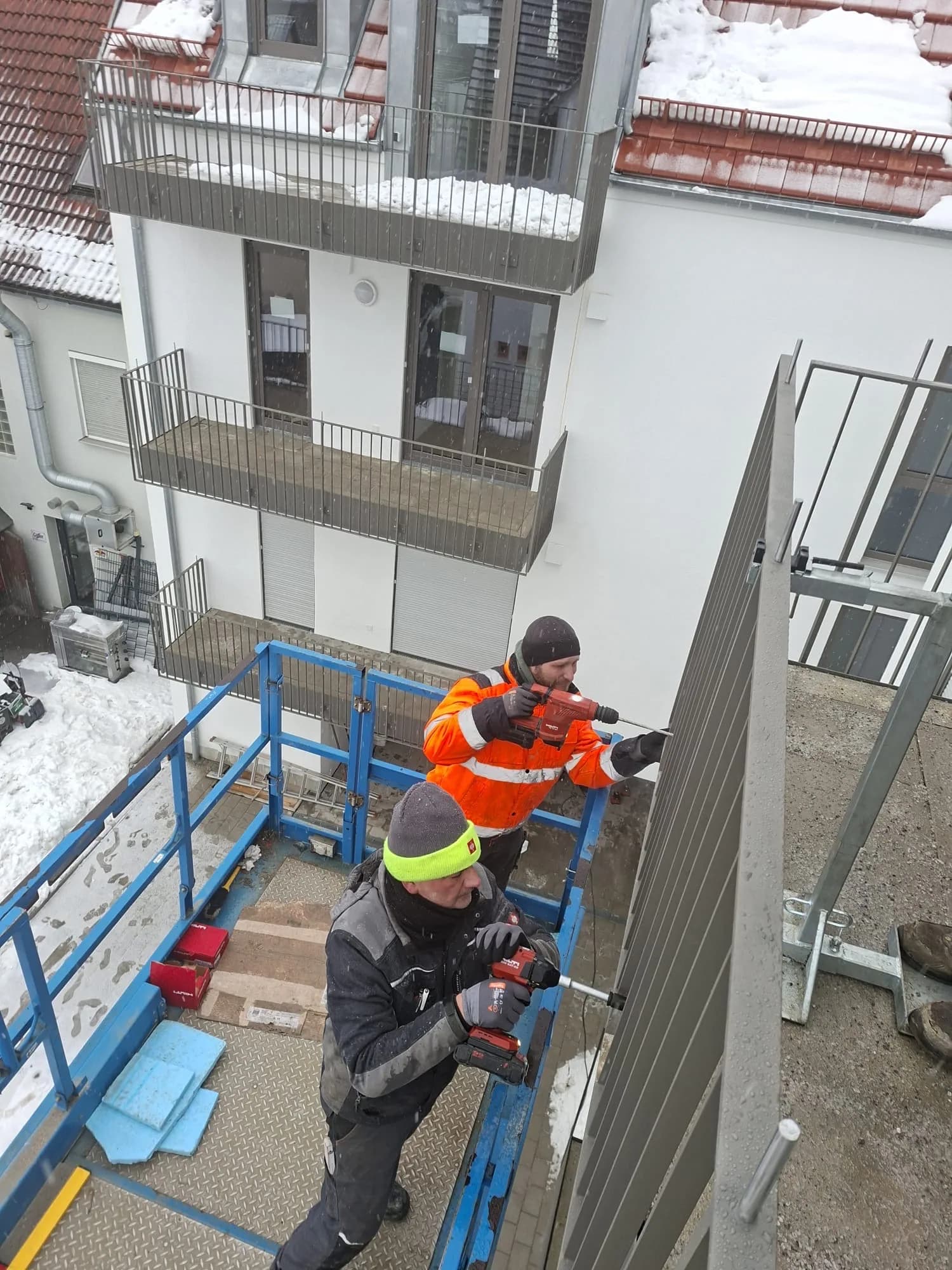 Zwei Monteure montieren mit Akkubohrmaschinen ein Balkongeländer bei Schneefall